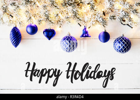 Banner di natale con la calligrafia Inglese Buone Vacanze. Abete del ramo con palle blu. Bianco sullo sfondo di legno e le luci fairy Foto Stock