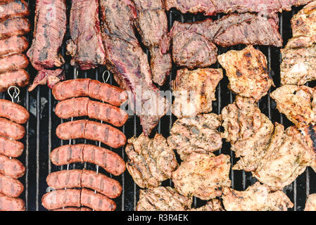 Salsicce, carne di maiale e di pollo arrostito su un barbecue, visto da sopra. Foto Stock