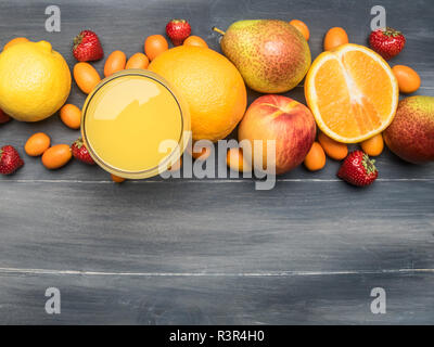 Delizioso assortimento di nuove varietà di frutti rivestita intorno con un bicchiere di succo di frutta, kumquat, fragole, arance, pera, limone, su un rustico in legno backgro Foto Stock