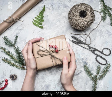 Ragazza esegue il wrapping di un regalo per un nuovo anno o il Natale accanto ad essa è un rotolo di carta, forbici vintage, ramoscelli di alberi di Natale e le bacche del Monte Ceneri, Foto Stock