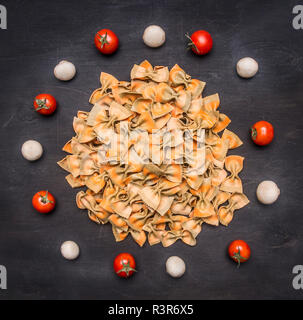 Materie pasta italiana con pomodorini, funghi e burro, foderati round su un rustico sfondo di legno Foto Stock