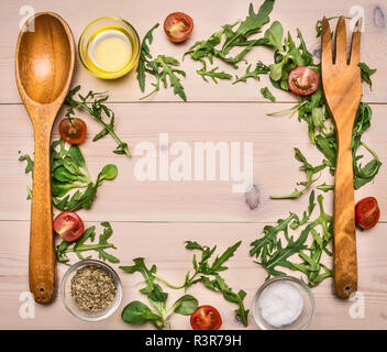 Forcella di legno e cucchiaio, rucola e altri ingredienti per la cottura di fresca insalata sana foderato con un telaio su una bianca tavolo in legno spazio per il testo Foto Stock