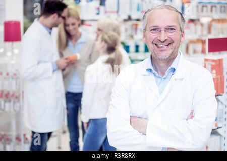 Ritratto di maschio maturo farmacista in piedi in farmacia, con i colleghi e i clienti in background. Foto Stock
