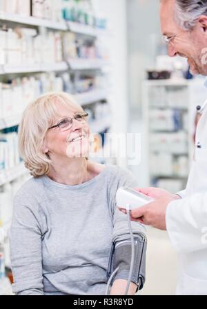 Il farmacista maschio controllo sorridente femmina senior di pressione del sangue del paziente in farmacia. Foto Stock