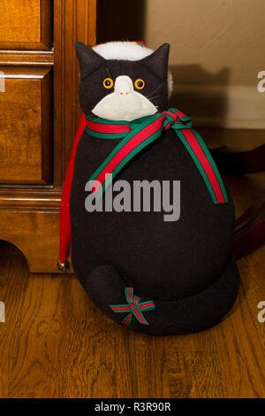 Una festosa farcite gatto nero che indossa un cappello da Babbo Natale e una vacanza sciarpa siede su un pavimento di legno. Foto Stock