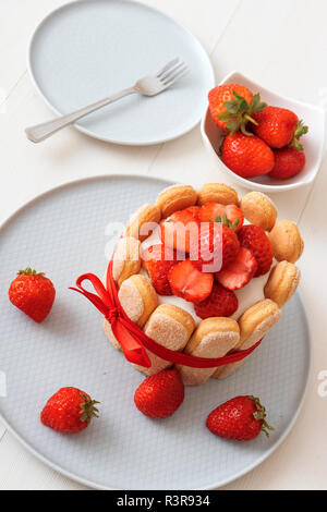 Charlotte, francese dessert con fragole, legato con un nastro rosso scarlatto, tazza di caffè, la ciotola con le fragole sul tavolo bianco. No-bake dessert. Top vi Foto Stock