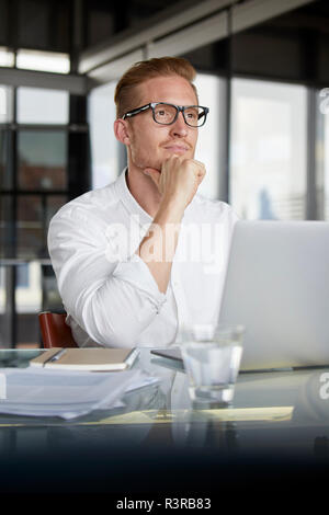 Imprenditore con laptop sulla scrivania in ufficio pensando Foto Stock