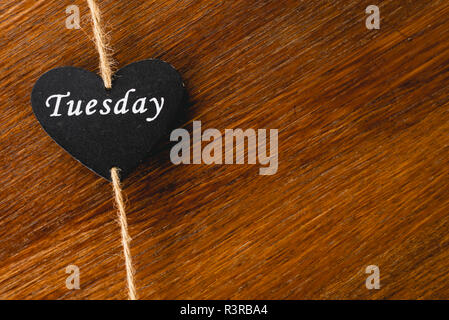 Cuore di legno nero con il giorno della settimana scritto su di esso, Martedì Foto Stock