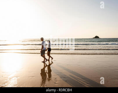 Coppia giovane fare una romantica passeggiata sulla spiaggia al tramonto Foto Stock