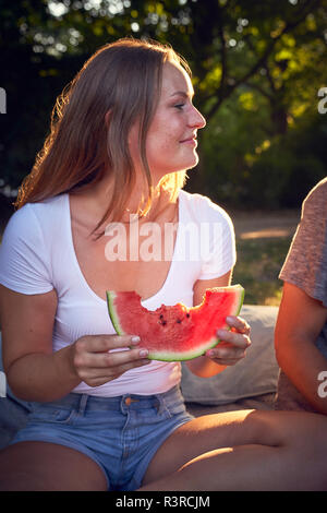 Coppia giovane seduto nel parco, mangiando anguria Foto Stock