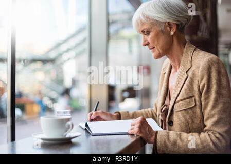 Senior imprenditrice prendendo appunti in un cafe Foto Stock