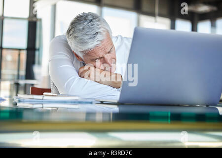 Imprenditore esausto dorme nella parte anteriore del computer portatile Foto Stock