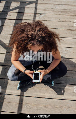 Atletica Giovane donna seduta sul Boardwalk utilizza lo smartphone Foto Stock