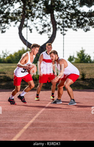 Tre giovani uomini giocare a basket su un tribunale aperto Foto Stock
