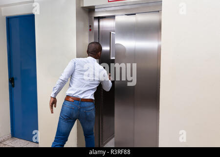 Vista laterale di un giovane africano arresto ascensore porta con la sua mano Foto Stock