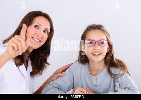 Femmina felice all'ottico optometrista puntare il dito mentre si verifica la visione degli occhi di una ragazza Foto Stock