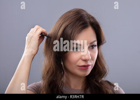 Close-up di una giovane donna pettinare i capelli su sfondo grigio Foto Stock