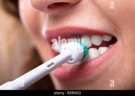 Close-up di una donna di mano spazzolare i denti con spazzolino da denti elettrico Foto Stock