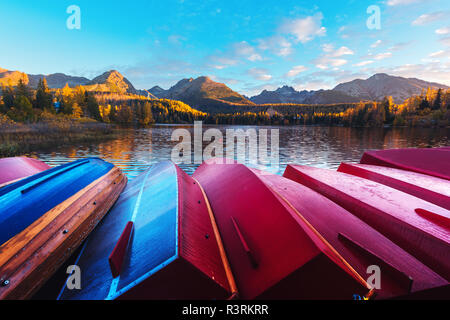 Pittoresca vista autunnale del lago il villaggio di Strbske Pleso negli Alti Tatra National Park, Slovacchia. Riga rossa di barche in legno e di alte montagne sullo sfondo. Foto Stock