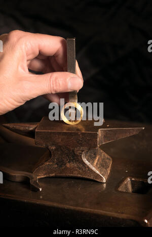 Goldsmith punzoni manuali un segno distintivo in un anello d'oro su una piccola incudine, copia dello spazio nel fondo scuro, selezionata la messa a fuoco e profondità di campo ridotta Foto Stock