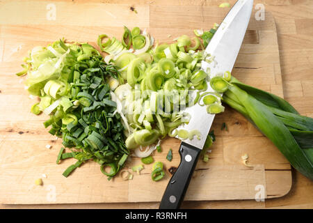 Tagliate a fette il porro e una grande cucina coltello su una tavola di legno, concetto di cucina a vista, elevato angolo vista da sopra Foto Stock