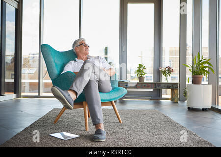 Uomo maturo rilassante in poltrona a la finestra a casa Foto Stock