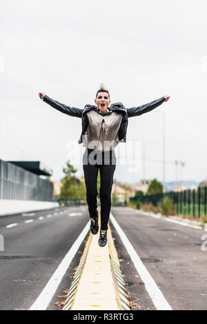 Donna Punk urlando e saltando su una barriera al bordo della strada Foto Stock