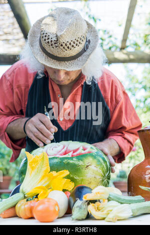 Senior uomo al lavoro su un cocomero con carving tool Foto Stock