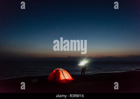 Giovane uomo camping sulla spiaggia, utilizzando la torcia elettrica Foto Stock