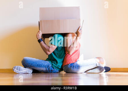 Giovane con teste in una scatola di cartone seduta di schiena sul pavimento a nuova casa Foto Stock