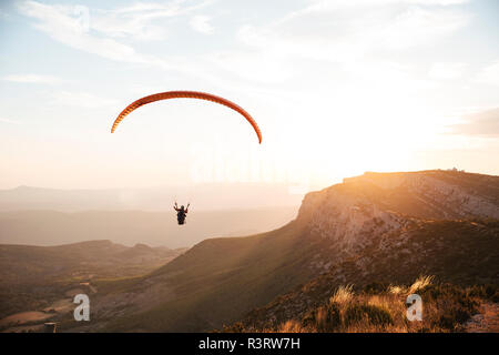 Spagna, Silhouette di parapendio volare alto sopra le montagne al tramonto Foto Stock