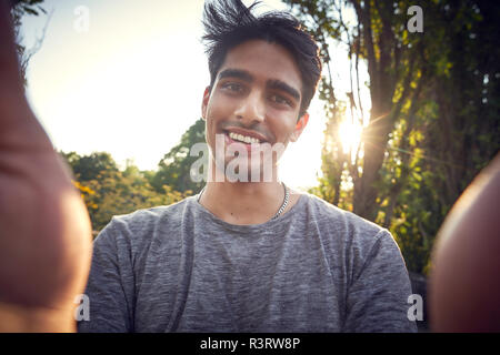 Ritratto di un giovane uomo in un parco al tramonto, tenendo selfie Foto Stock