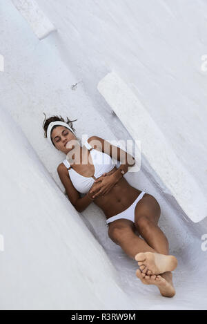 Giovane donna indossa bikini bianco giacente in una nicchia della parete, vista dall'alto Foto Stock