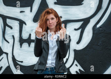 L'Italia, Finale Ligure, ritratto di redheaded ragazza adolescente che mostra il dito nella parte anteriore della parete con cranio graffito Foto Stock