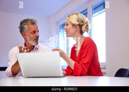 Due colleghi con il portatile a scrivania in ufficio discutendo Foto Stock