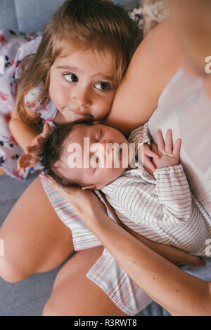 Madre tenendo il suo bambino vicino con la sorella sensazione i suoi capelli Foto Stock