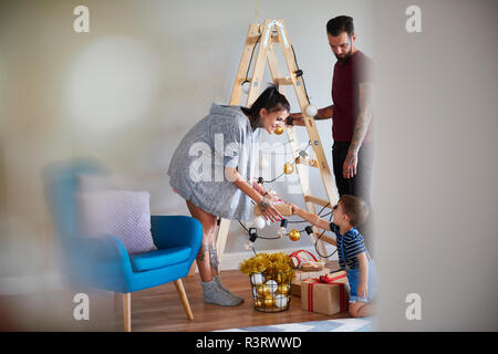 Famiglia moderna a casa al tempo di Natale utilizzando la scala come albero di Natale Foto Stock