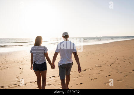 Coppia giovane fare una romantica passeggiata sulla spiaggia al tramonto Foto Stock