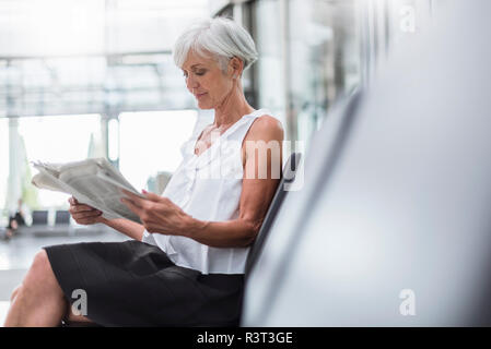 Senior donna seduta nella zona di attesa quotidiano di lettura Foto Stock