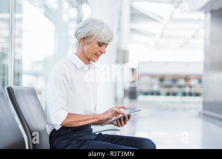 Senior imprenditrice seduta in area di attesa utilizzando tablet Foto Stock