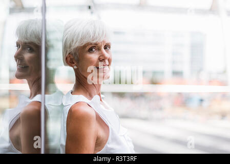 Ritratto di sorridente donna senior appoggiata contro la facciata di vetro Foto Stock