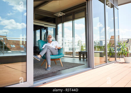 Uomo maturo rilassante in poltrona a terrazza sul tetto di casa Foto Stock