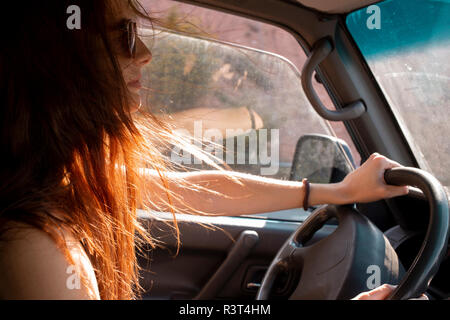 Giovane donna con capelli spazzate dal vento alla guida di una macchina Foto Stock