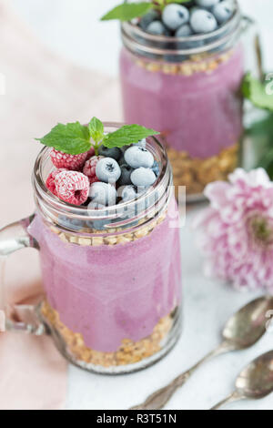 Due bicchieri di yogurt con muesli di arachidi, aronia polvere e topping di nocciole e bacche smerigliato Foto Stock