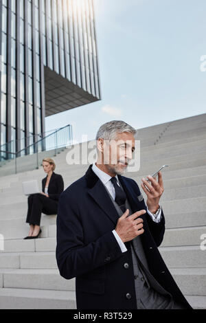 Ritratto di imprenditore a parlare al telefono mentre business donna lavora sul computer portatile in background Foto Stock