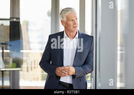 Imprenditore preoccupato in piedi dalla finestra, pensando Foto Stock