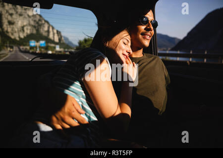 Sorridente affettuoso coppia giovane seduto sul sedile posteriore di una macchina Foto Stock