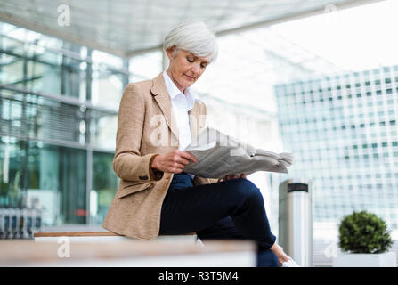 Senior imprenditrice seduta nella città giornale di lettura Foto Stock