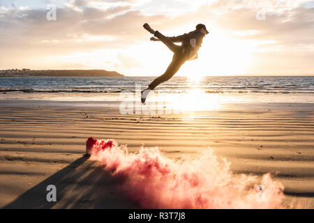 Uomo che fa del movimento di formazione presso la spiaggia con fumo colorato al tramonto Foto Stock