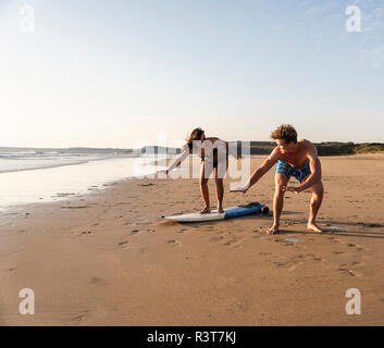 Giovane uomo che mostra giovane donna come navigare sulla spiaggia Foto Stock